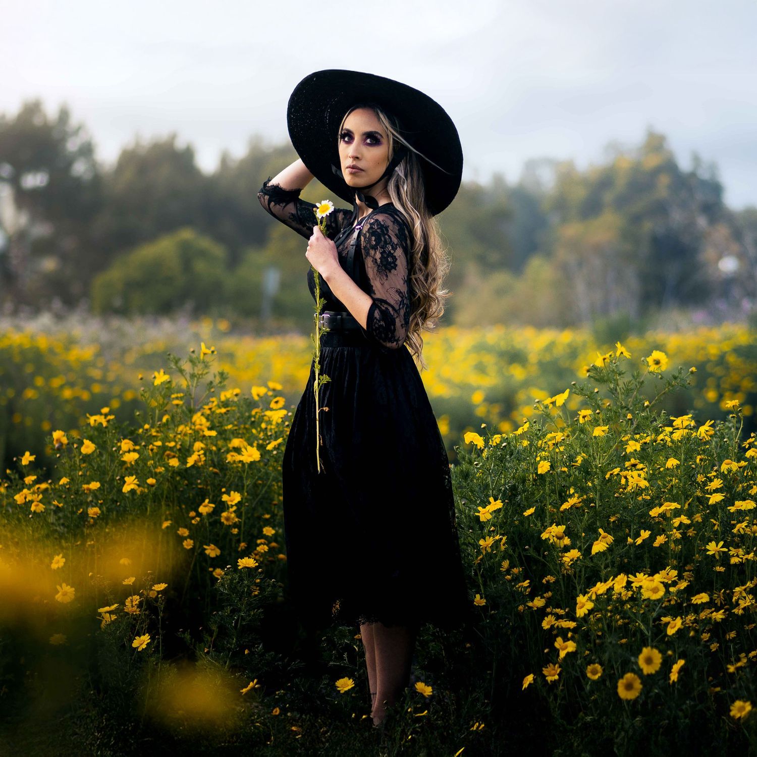 Model dressed in all black poses in a field of blooming yellow flowers during spring in Huntington Beach, captured by Chris Cornish Photogra