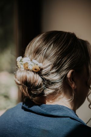 Elegant bridal updo hairstyle adorned with small white and yellow wildflowers, photographed from behind.