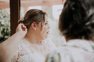 Bride in lace dress having hair styled by bridesmaid before wedding ceremony.