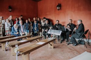 A small ensemble performs for a crowd in a rustic red-walled venue with wooden benches during an intimate concert.