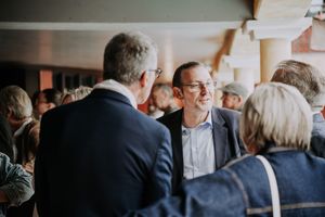 Professionals networking at an indoor event, engaged in conversation in a crowded venue.