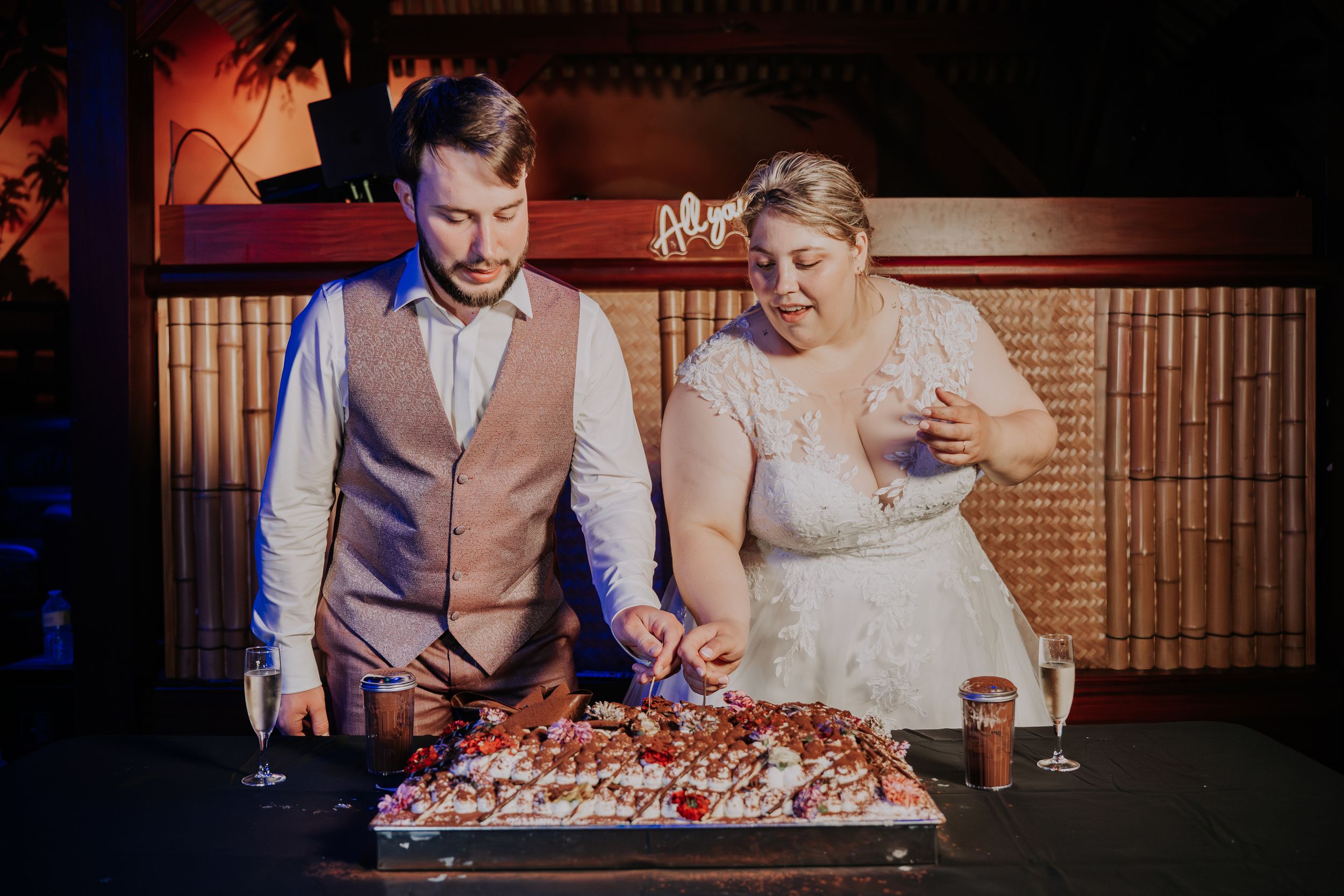 Bride and groom cutting their wedding cake together at a warmly lit reception venue.
