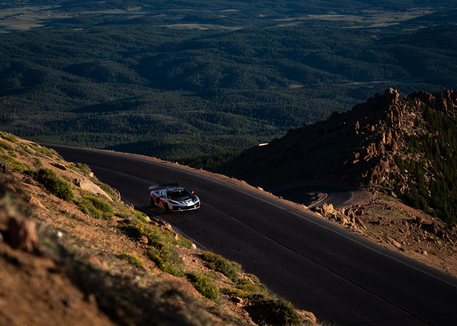 Race car navigating a winding mountain road at Pikes Peak with sweeping forested valley views below.