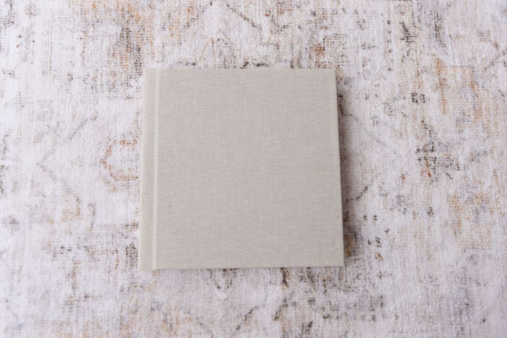 A minimalist linen-covered photo album in neutral gray on a distressed white background.