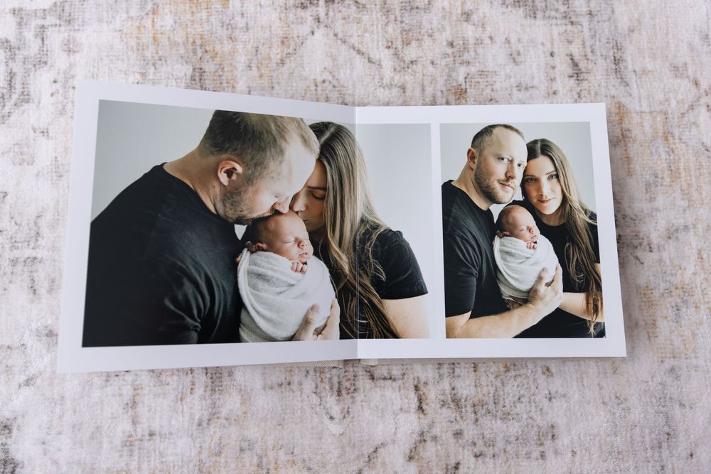 An open photo album displaying newborn baby portraits with parents on a textured surface.