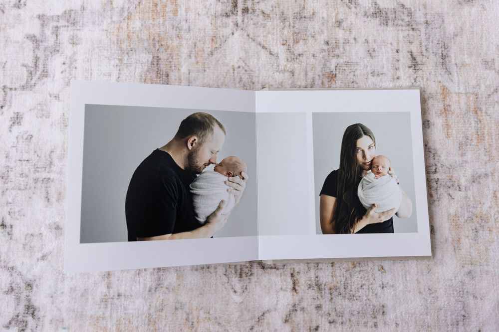 An open photo album featuring tender portraits of parents individually holding their newborn baby.