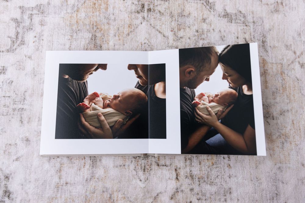 An open photo album showing intimate black and white newborn portraits of parents with baby.