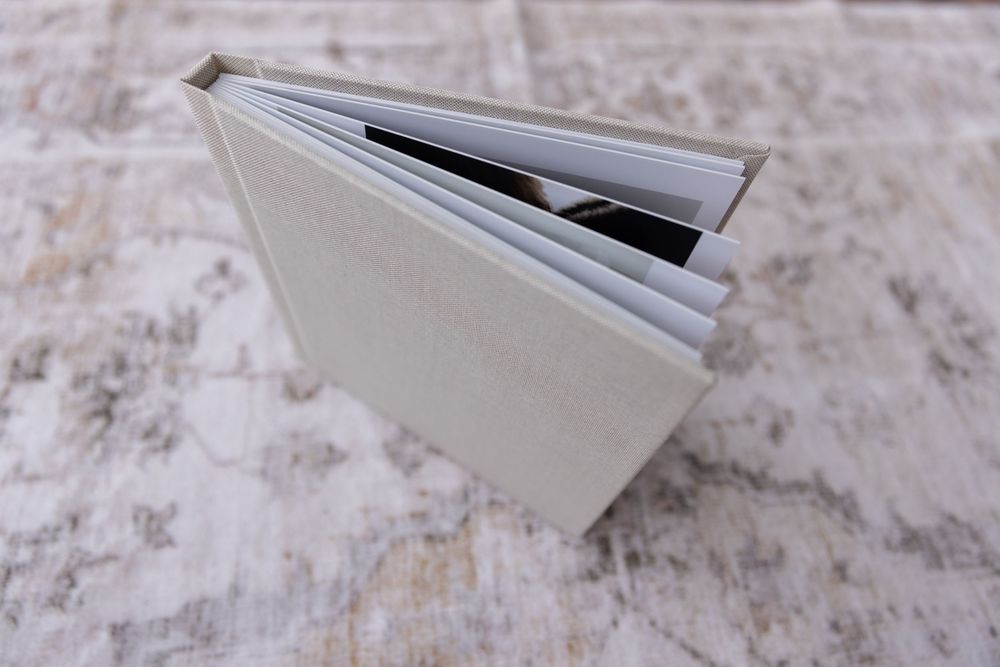 A linen hardcover photo album standing open showing thick lay-flat pages on textured surface.