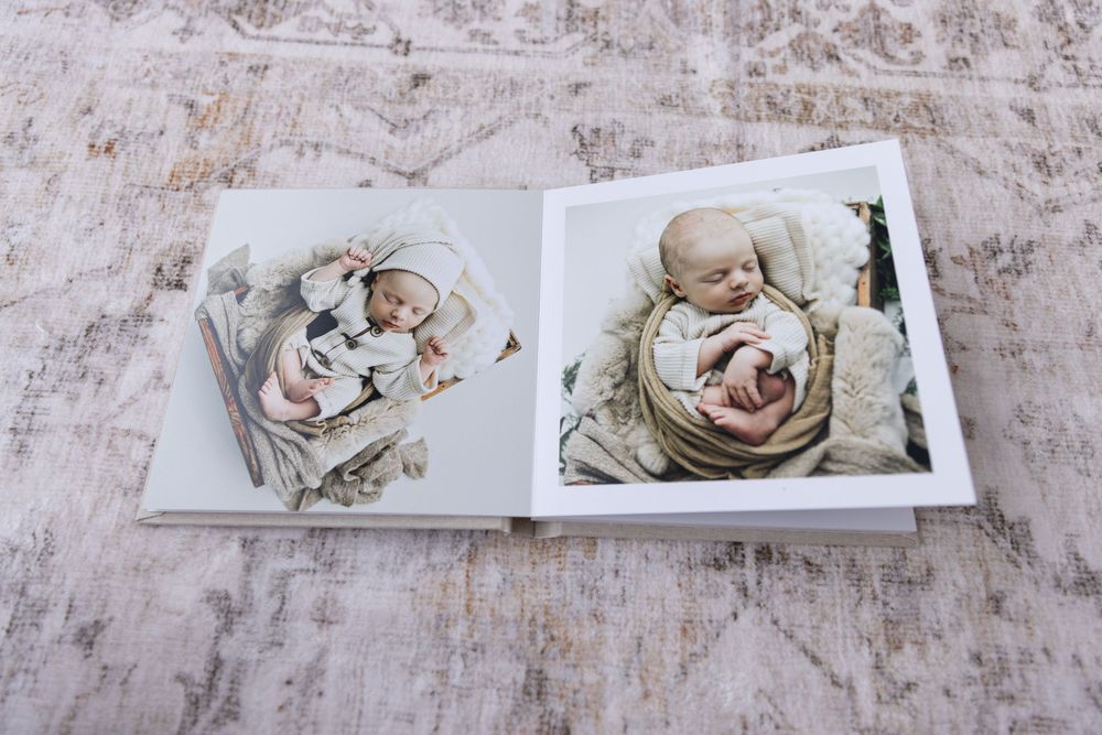 An open photo album displaying soft neutral-toned newborn baby portrait photographs side by side.
