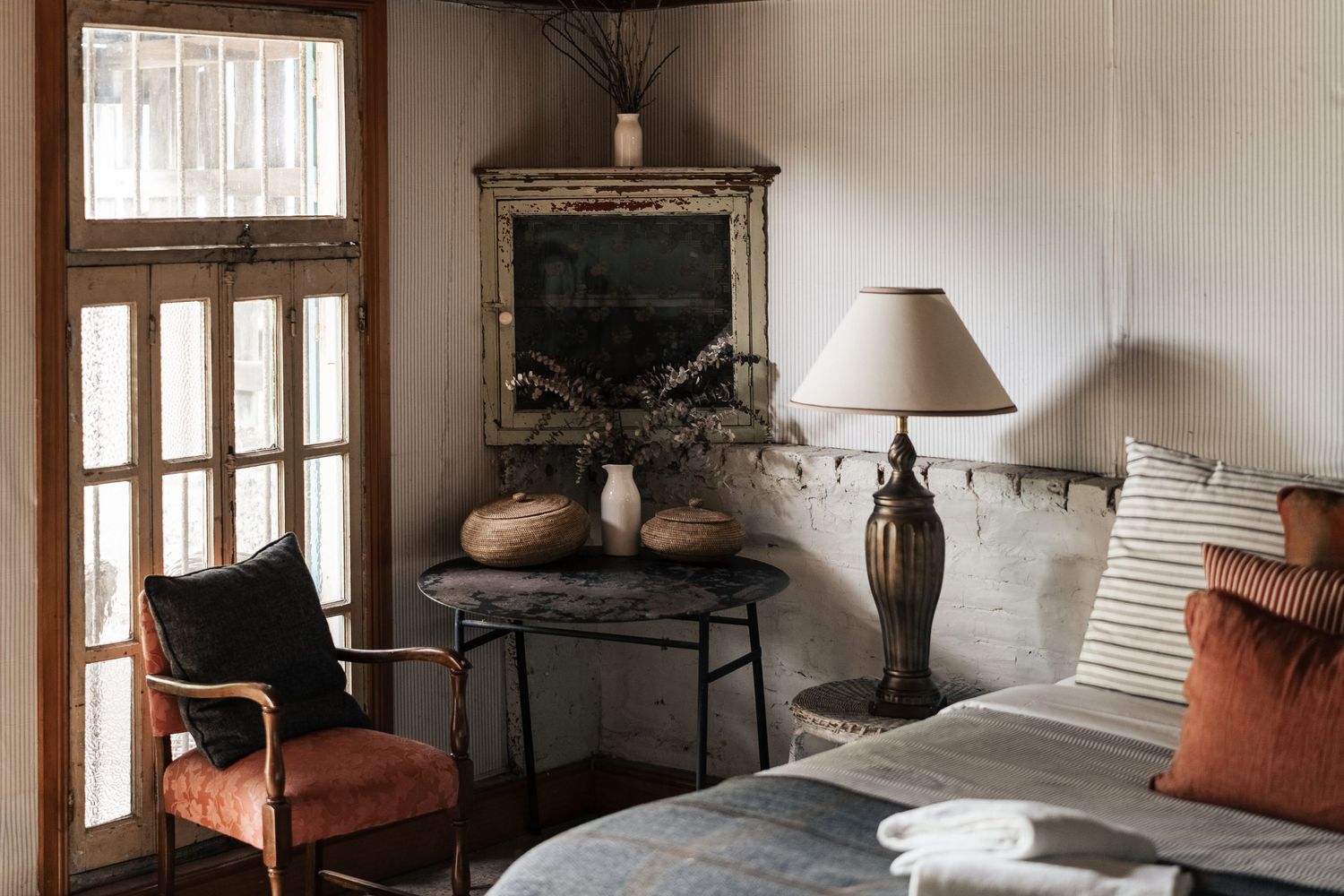 Rustic bedroom corner with vintage mirror, antique lamp, terracotta chair, and distressed decor.

The Barn