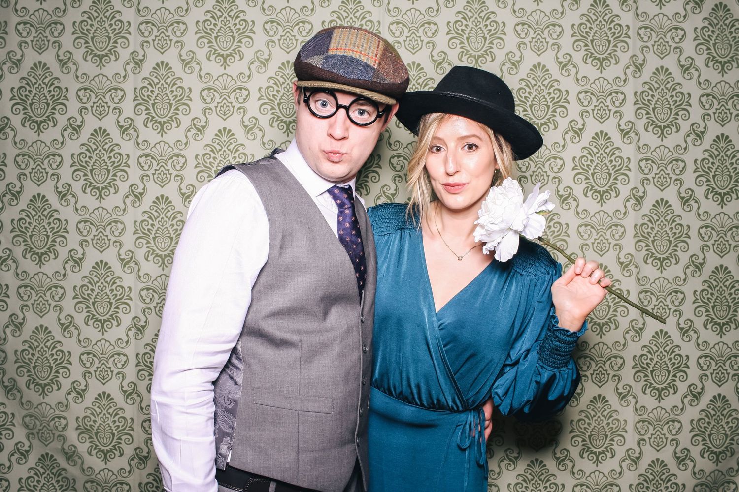 Three people in fun hats and accessories pose in front of red and white striped backdrop at a photo booth event.