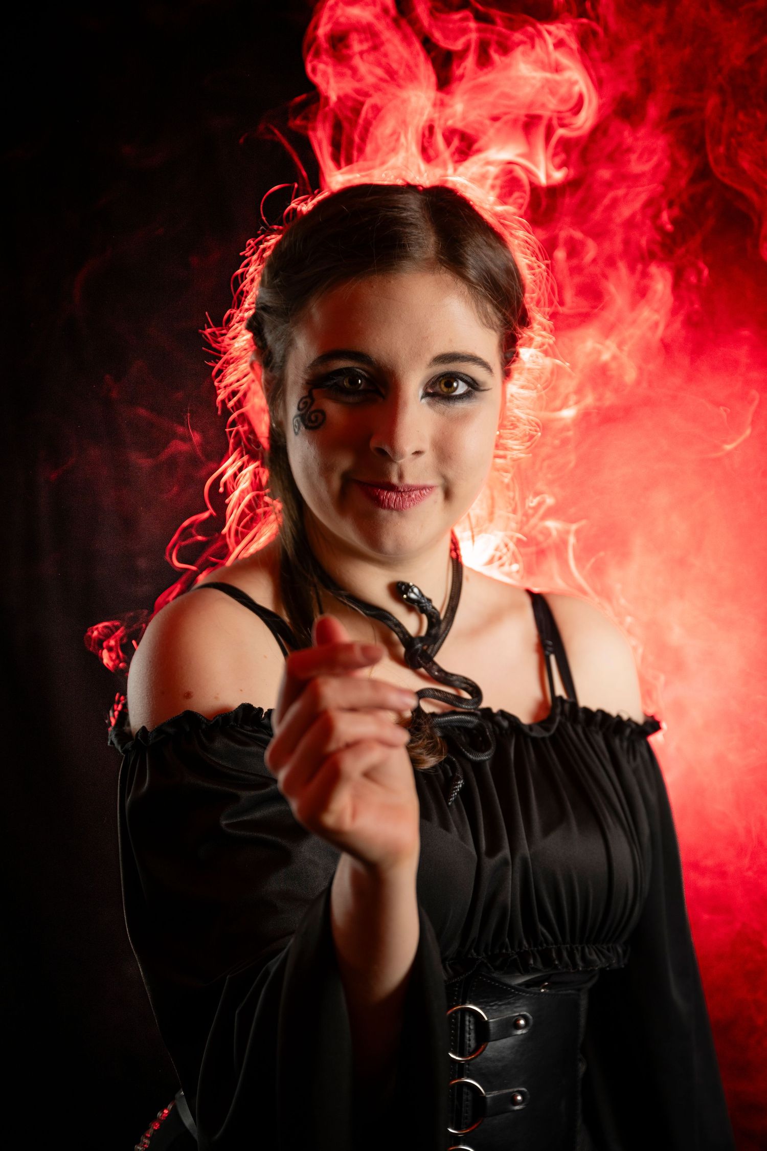 Woman in black corset dress with dramatic Halloween makeup poses with red smoke swirling behind her.