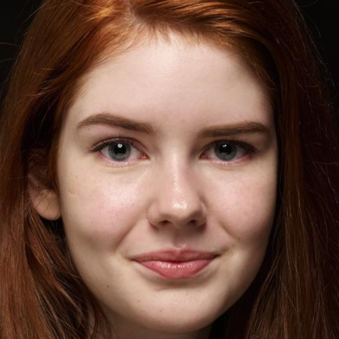 Young woman with long red hair and blue-gray eyes poses against a dark background with a subtle smile.