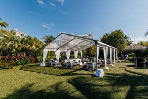 Elegant outdoor wedding reception under a white tent with draped fabric, surrounded by lush tropical greenery and palm trees.