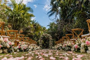 Romantic garden wedding aisle lined with pink and white roses and rose petals under palm trees.