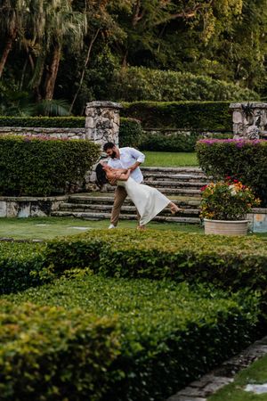 Couple sharing a romantic dip kiss in a lush formal garden with manicured hedges and stone steps.