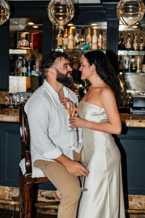 Couple sharing a romantic moment at an upscale bar, holding champagne glasses, dressed elegantly in white attire.