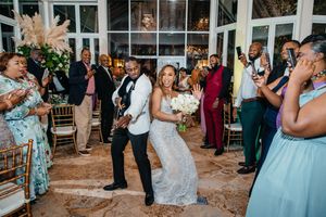 Bride and groom dance joyfully at wedding reception surrounded by celebrating guests in elegant venue.