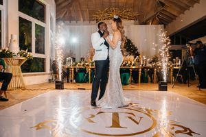 Couple shares first dance on monogrammed white floor with gold sparklers at elegant wedding reception.