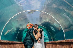 Bride and groom sharing a romantic kiss inside an aquarium tunnel with sharks swimming overhead.