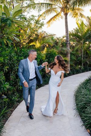 Happy couple walking hand in hand along a tropical garden path at golden hour wedding celebration.