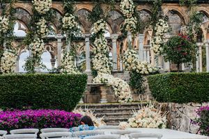 Luxurious wedding altar adorned with cascading white flowers and lush greenery against ornate stone arches.