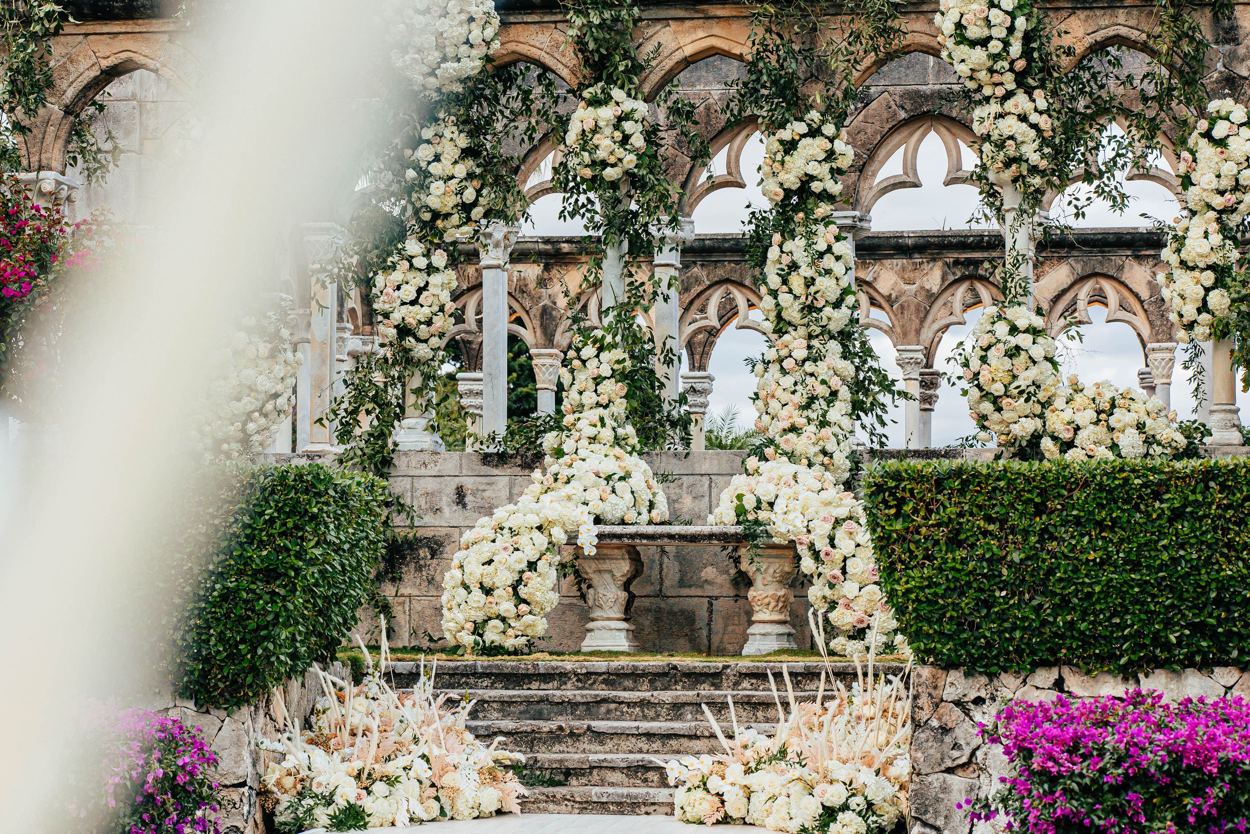 Elegant wedding ceremony setup with white floral arches and arrangements on stone steps at a luxury villa.