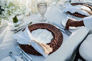 Elegant wedding table setting with wicker charger plates, crystal glasses, and white napkins.