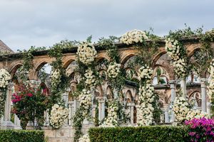 Stunning white floral displays covering gothic stone arches at a luxurious outdoor wedding venue.