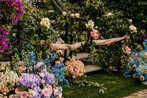 Romantic garden wedding setup featuring colorful floral arrangements and a wooden swing draped with fabric.