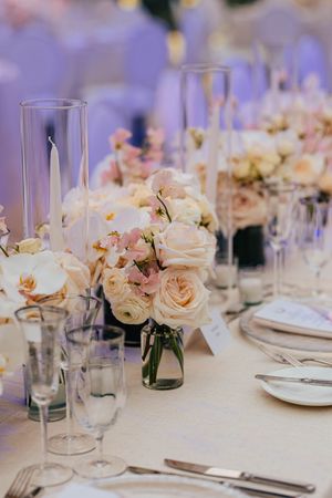 Romantic wedding reception table with blush roses, orchids, tall candles, and crystal glassware.