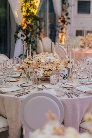 Elegant wedding reception table with blush rose centerpiece, crystal glassware, tall candles, and white orchid arrangements.