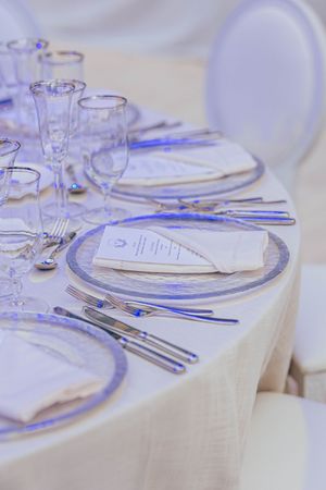 Elegant wedding reception table set with blue-rimmed glass plates, crystal stemware, silver cutlery, and white linen napkins.