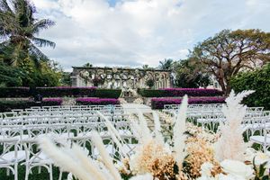 Outdoor wedding venue with white chairs, pampas grass, colorful hedges, and historic stone ruins.