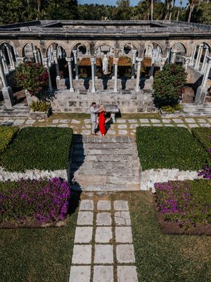 Aerial view of a couple in a formal garden with stone colonnades, statues, hedges, and colorful flowers in the Bahamas.