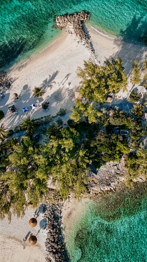 Aerial view of a tropical island with turquoise waters, white sandy beach, and lush green palm trees.