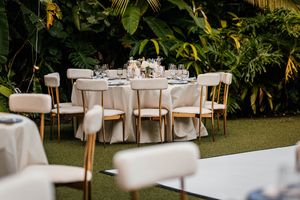 Elegant outdoor wedding reception table set with white linens and chairs amid lush tropical greenery.