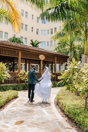 Bride and groom walking hand in hand through a tropical garden pathway at a resort wedding venue.