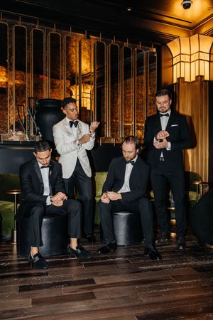 Groom in white tuxedo with groomsmen in black tuxedos adjusting cufflinks in a glamorous venue.