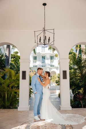 Bride and groom embrace under elegant chandelier archway surrounded by lush tropical greenery at luxury resort wedding venue.
