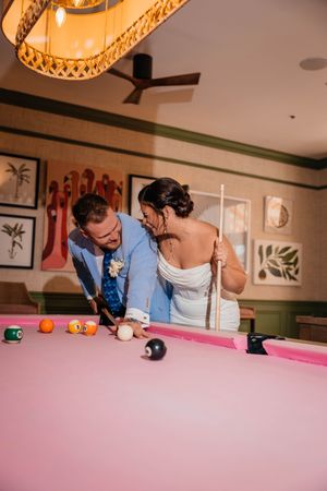 Bride and groom playing pool on a pink billiard table at their wedding reception venue.