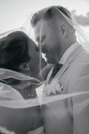 Black and white photo of bride and groom sharing intimate moment under wedding veil.