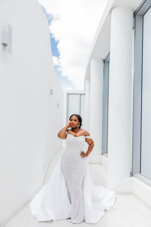Bride in sparkling off-shoulder mermaid gown with train poses in modern white architectural space.