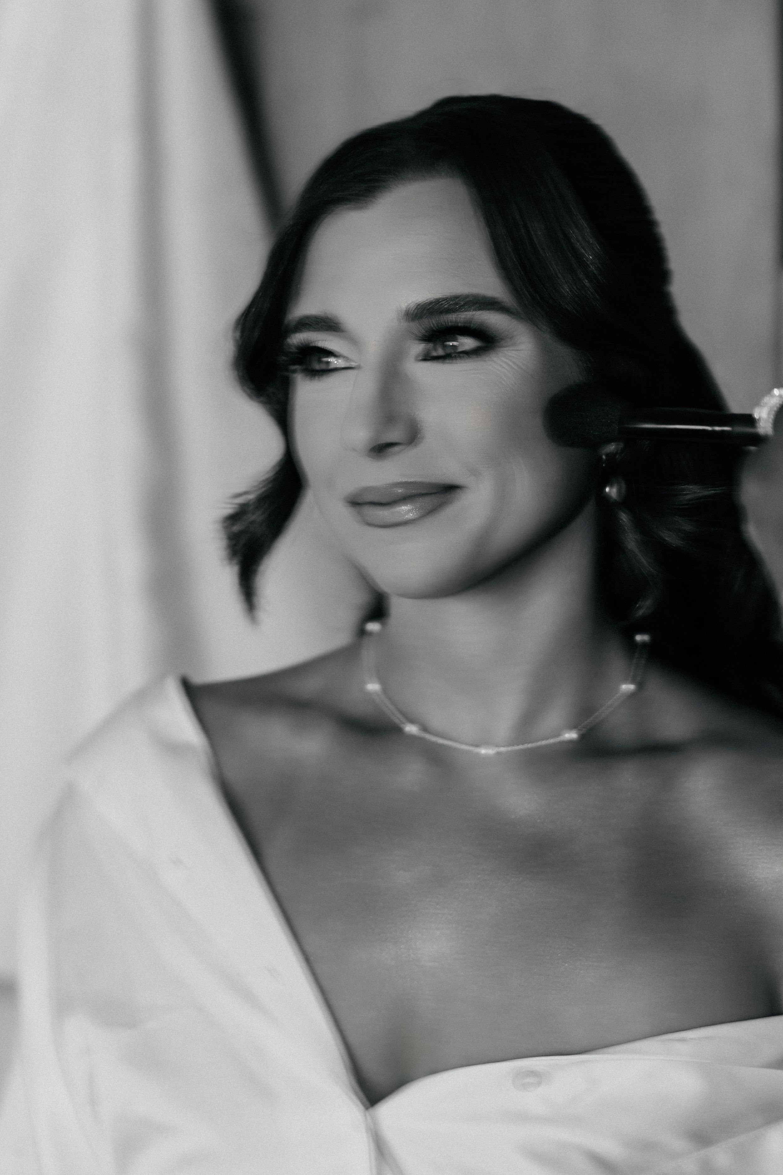 Black and white portrait of a beautiful bride getting makeup done wearing a pearl necklace.