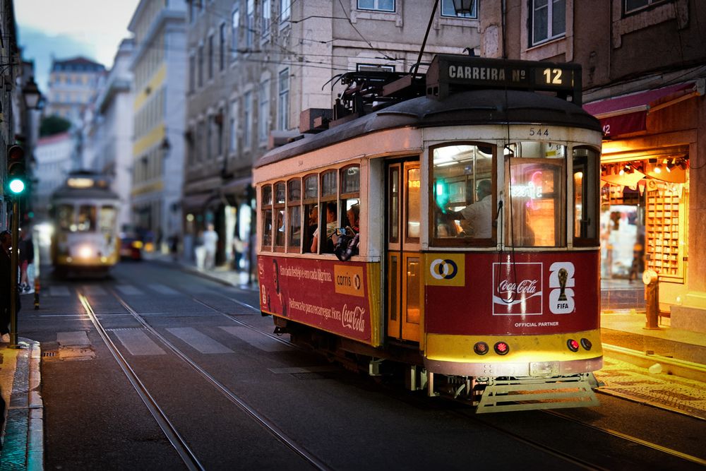 Vintage red tram number 12 on a cobblestone street in Lisbon, Portugal, illuminated at dusk.