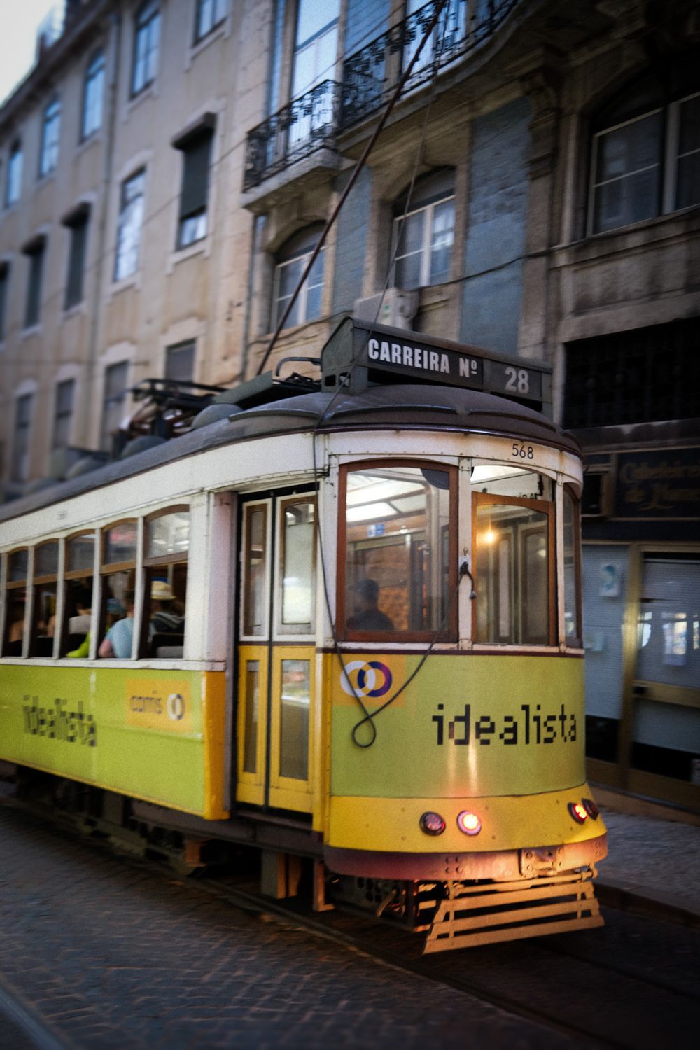 Yellow tram number 28 with Idealista branding on a narrow Lisbon street at dusk.