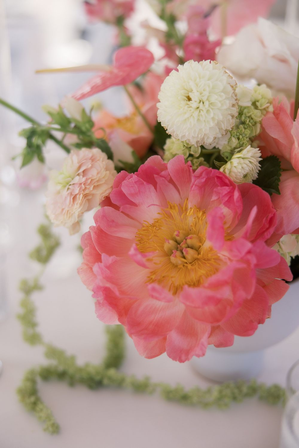 Pink peony and white flower bouquet arrangement in white vase with green garland on white table.