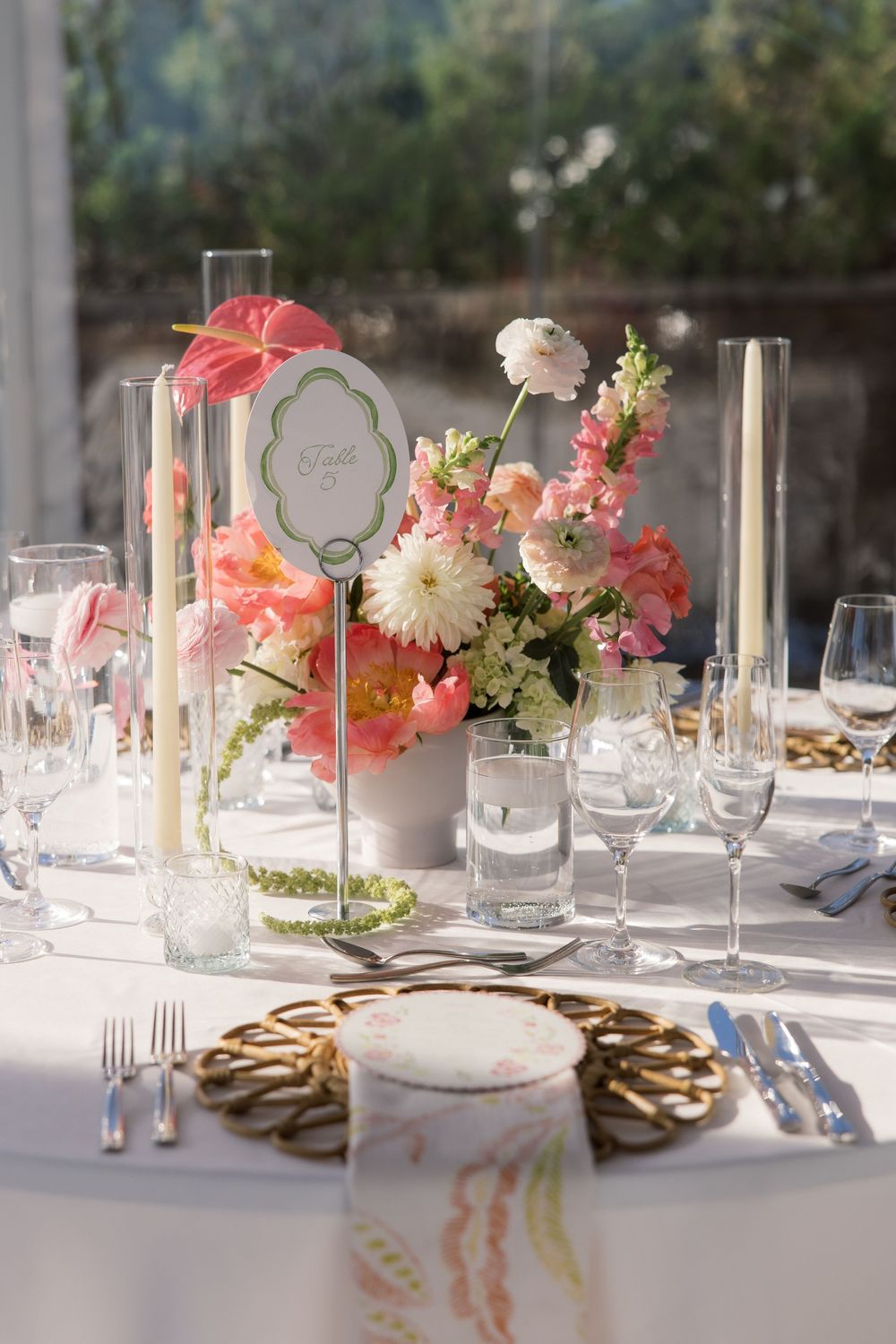 Elegant wedding table setting with pink floral centerpiece, tall candles, gold charger plates, and crystal glassware.