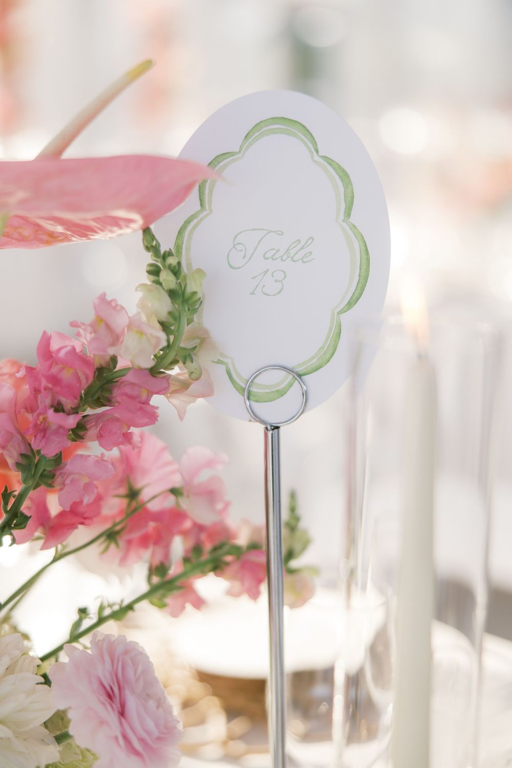 Elegant wedding table number 13 card on silver stand surrounded by pink flowers and greenery.