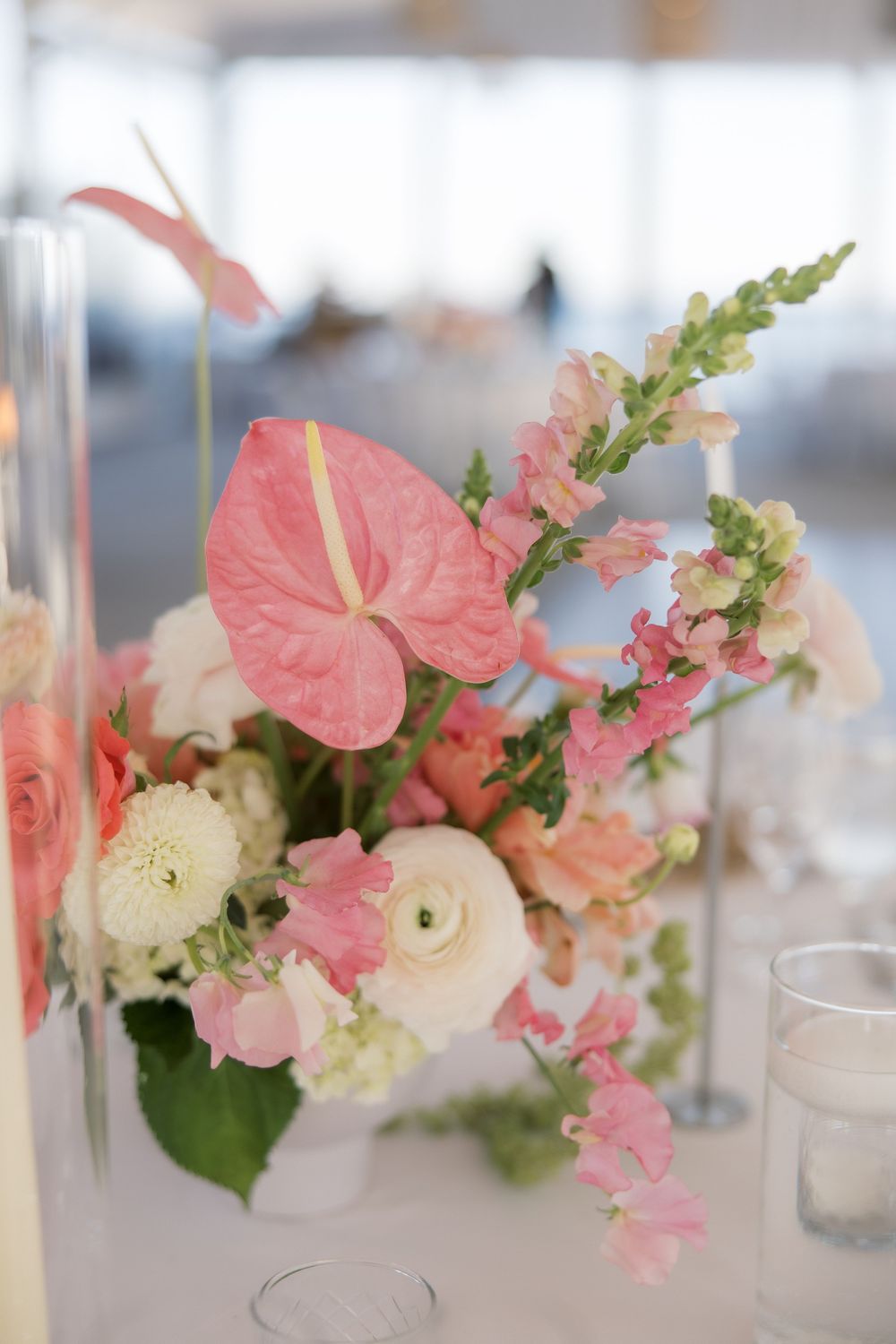 Pink anthurium and ranunculus floral centerpiece with snapdragons on a white table at an elegant wedding reception.
